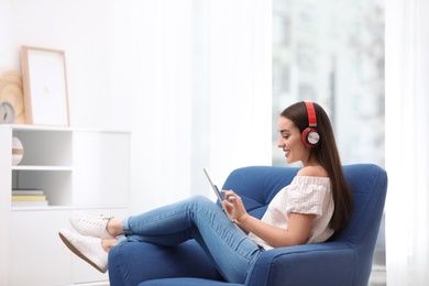 Young woman with headphones and tablet sitting in armchair at home