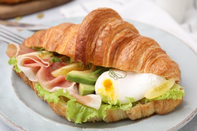 Photo of Delicious croissant with prosciutto, avocado and egg on white table, closeup