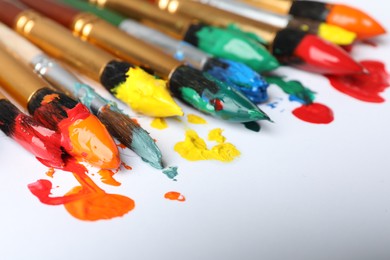 Photo of Brushes with colorful paints on white background, closeup