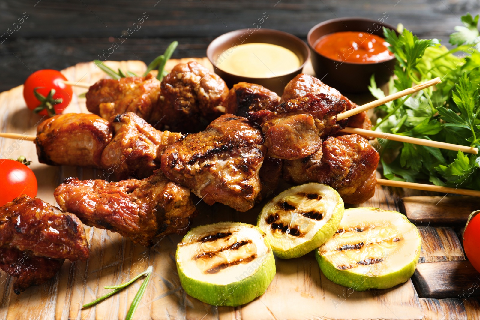 Photo of Delicious barbecued meat served with garnish and sauces on wooden board, closeup