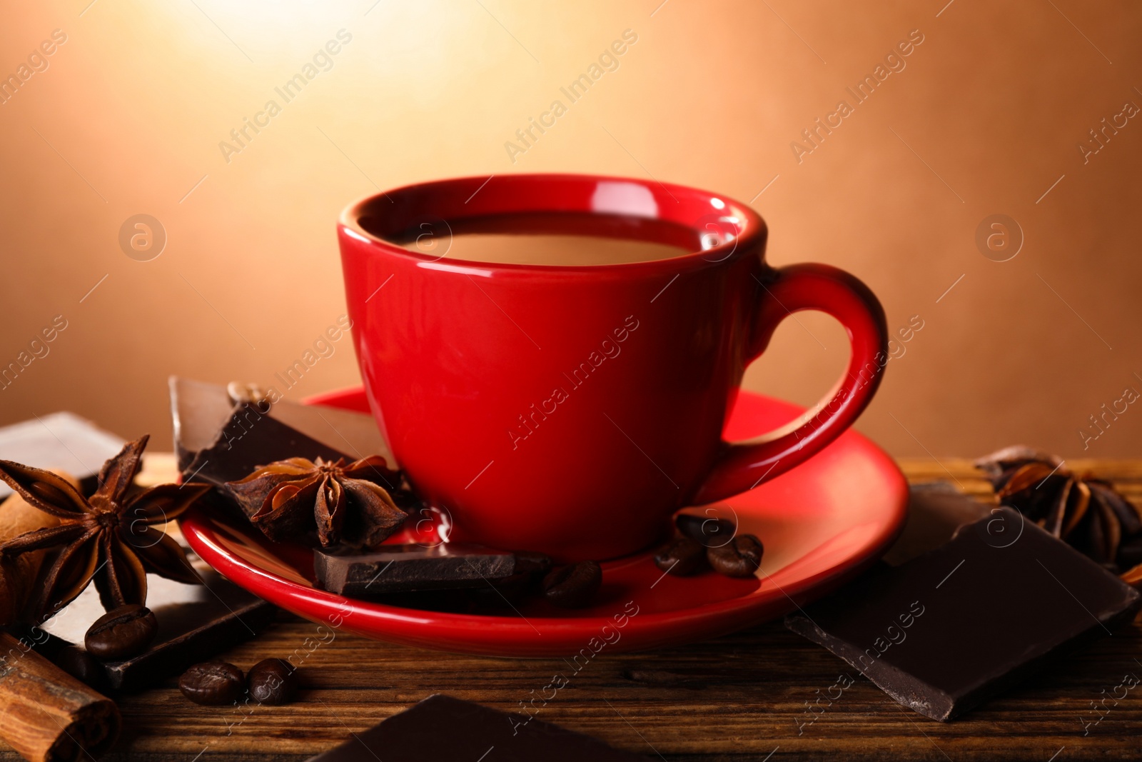 Photo of Cup of delicious hot chocolate, spices and coffee beans on wooden table