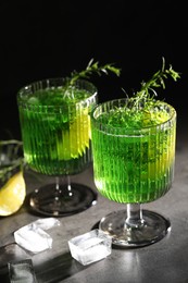 Photo of Glasses of homemade refreshing tarragon drink, ice cubes and sprigs on grey table