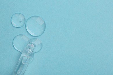 Photo of Dripping cosmetic serum from pipette onto light blue background, top view. Space for text