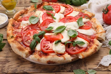 Photo of Delicious Caprese pizza with tomatoes, mozzarella and basil on wooden table, closeup