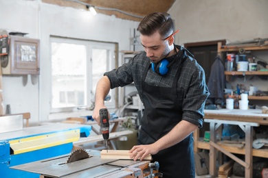 Photo of Young working man using electric screwdriver at carpentry shop