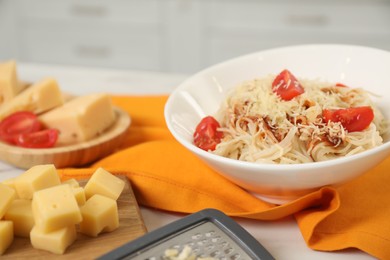 Photo of Delicious pasta with grated cheese and tomatoes on white table in kitchen, closeup