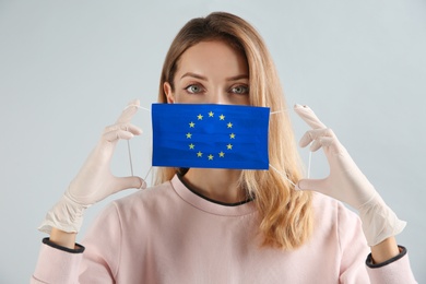 Woman wearing medical mask with European Union flag on light background. Coronavirus outbreak in Europe