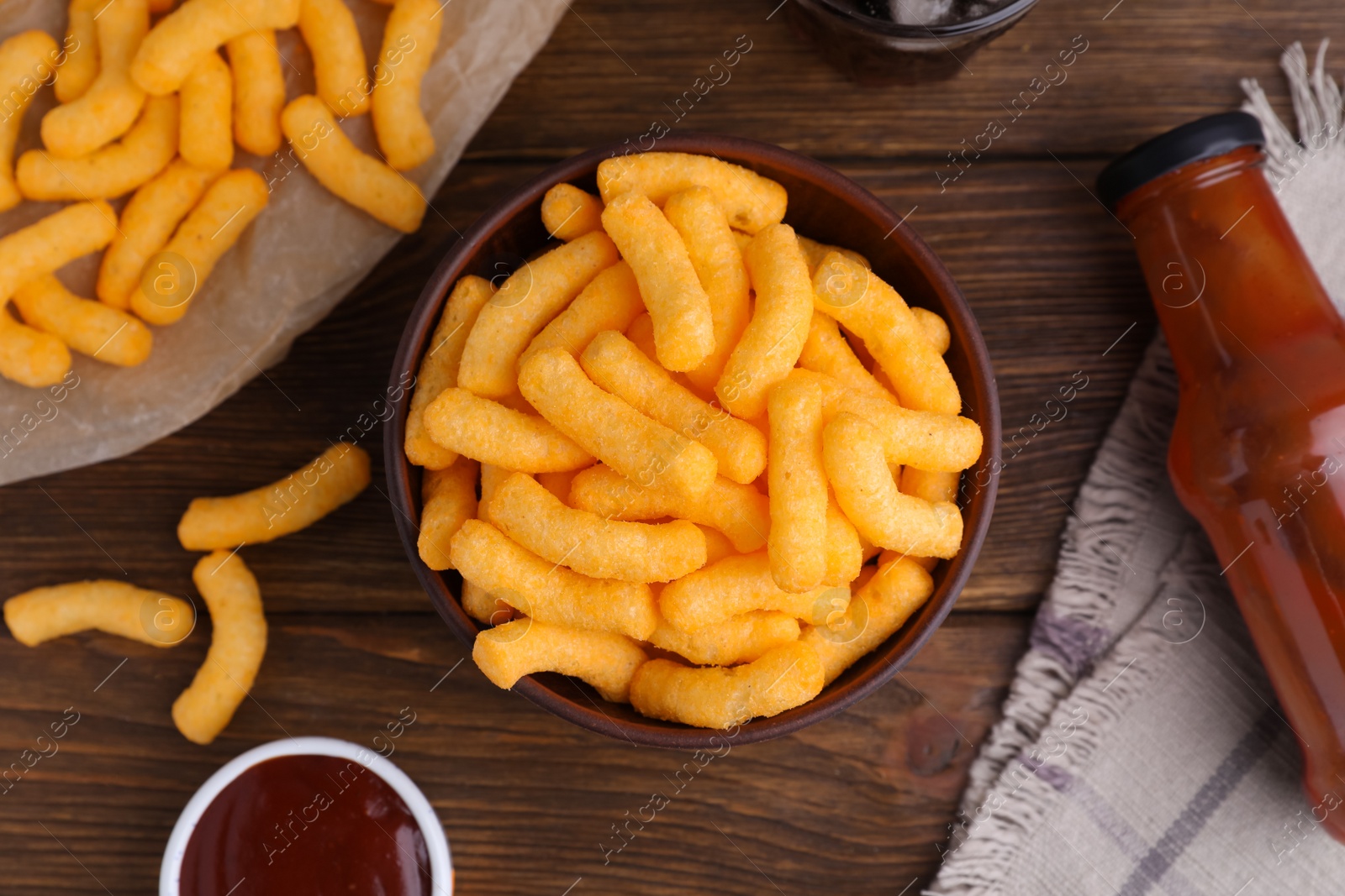 Photo of Crunchy cheesy corn snack and ketchup on wooden table, flat lay