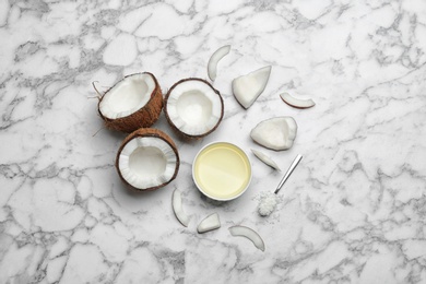 Photo of Bowl of natural organic oil and coconuts on marble background, flat lay