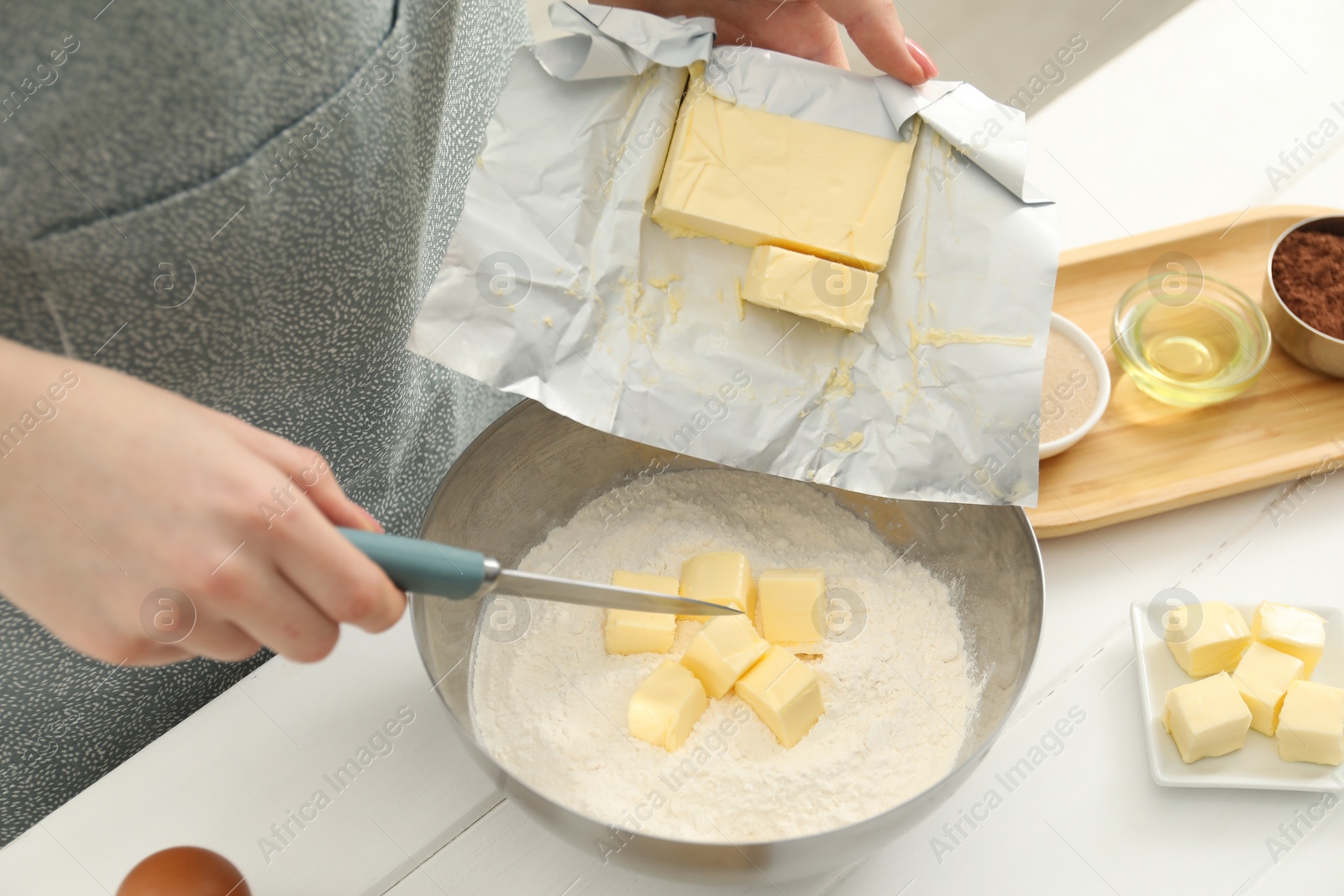 Photo of Woman adding fresh butter into bowl with flour at white wooden table, closeup