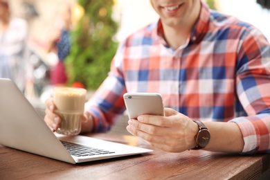 Young man using mobile phone while working with laptop at desk, closeup