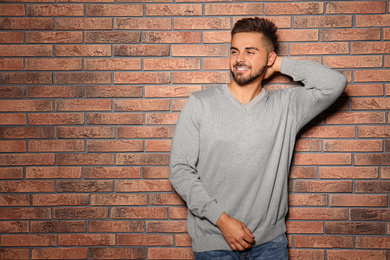 Handsome man wearing warm sweater near brick wall. Space for text