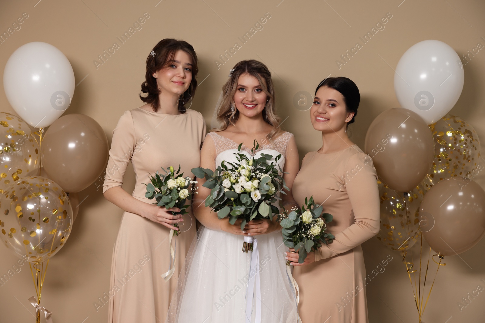 Photo of Happy bride and her bridesmaids with bouquets on beige background
