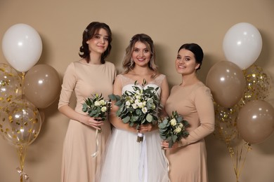 Happy bride and her bridesmaids with bouquets on beige background
