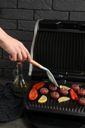 Photo of Woman cooking meat balls with bell pepper and lemon on electric grill at grey table, closeup