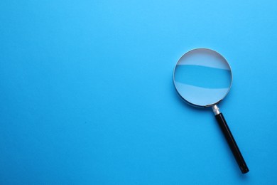 Photo of Magnifying glass on light blue background, top view. Space for text