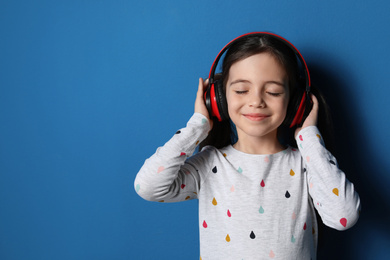 Cute little girl with headphones listening to audiobook on blue background. Space for text