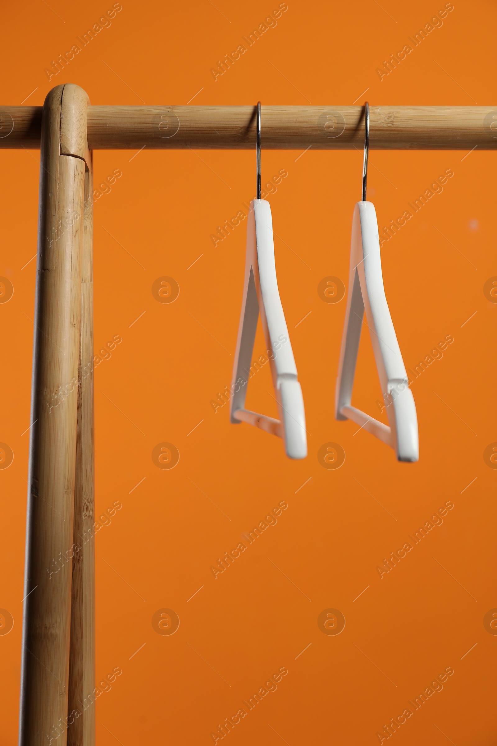 Photo of Empty clothes hangers on wooden rack against orange background