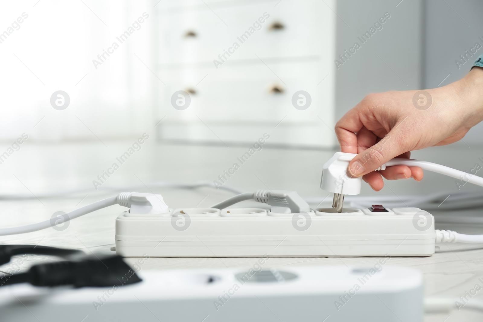 Photo of Woman inserting power plug into extension cord on floor indoors, closeup with space for text. Electrician's professional equipment