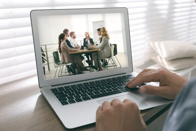 Man attending online video conference via modern laptop at table, closeup