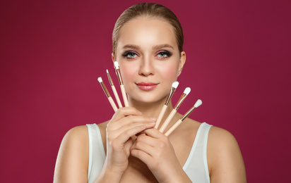 Beautiful woman with makeup brushes on pink background
