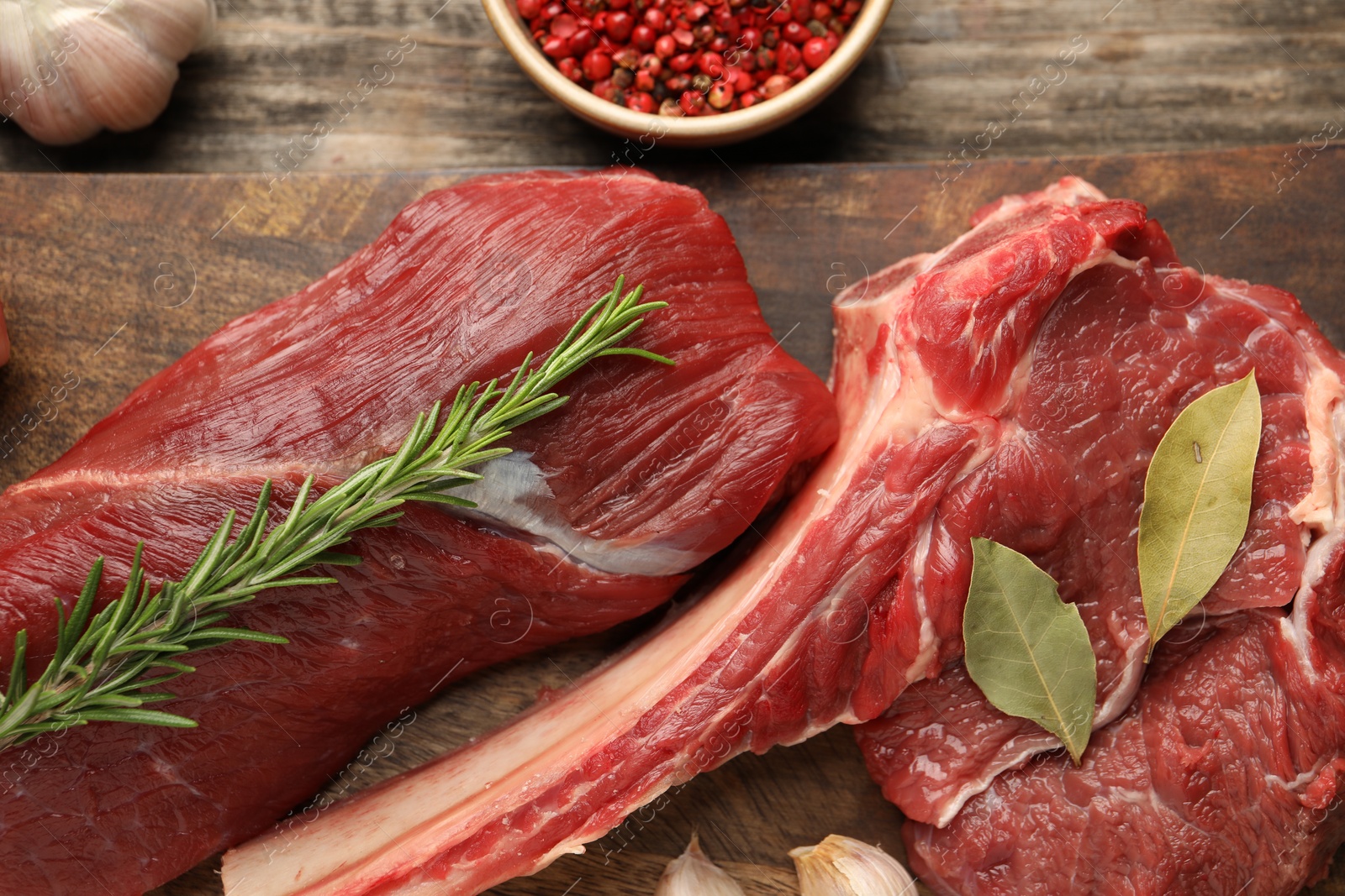 Photo of Pieces of raw beef meat and spices on wooden table, flat lay