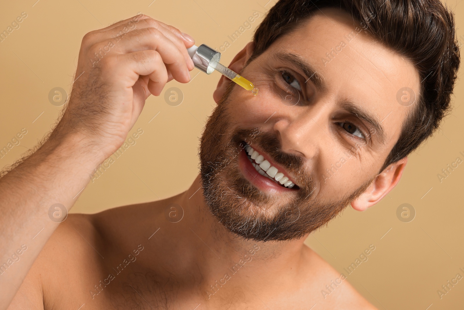 Photo of Smiling man applying cosmetic serum onto his face on beige background, closeup