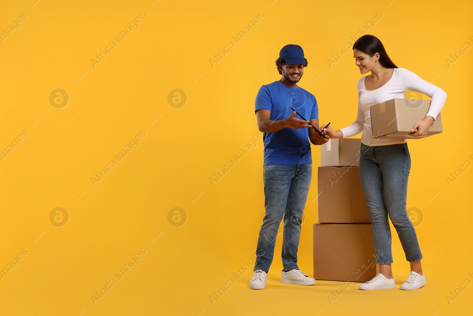 Photo of Smiling woman signing order receipt on orange background, space for text. Courier delivery