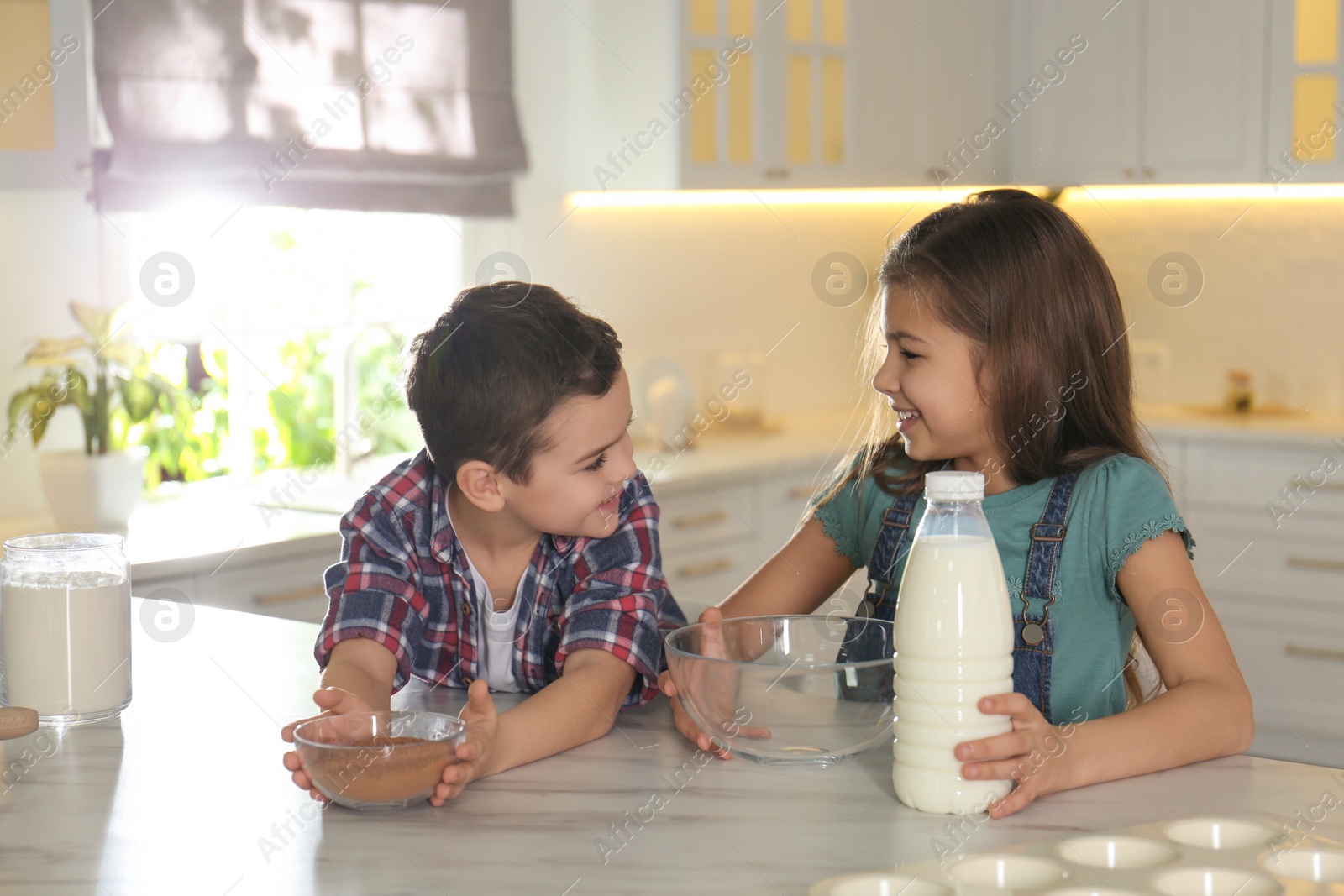 Photo of Cute little children at table with cooking ingredients in kitchen