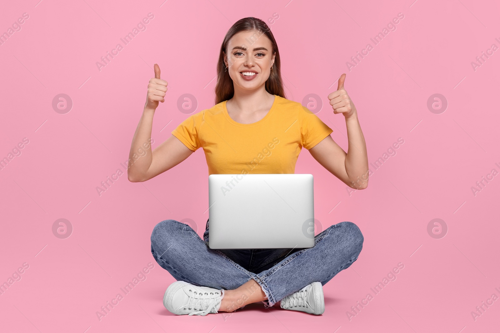 Photo of Happy woman with laptop showing thumbs up on pink background