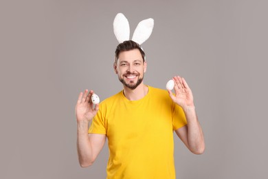 Photo of Happy man in bunny ears headband holding painted Easter eggs on grey background