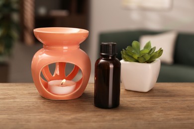 Photo of Aroma lamp with small candle, bottle of oil and houseplant on wooden table indoors