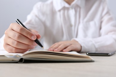 Woman writing in notebook at wooden table in office, closeup