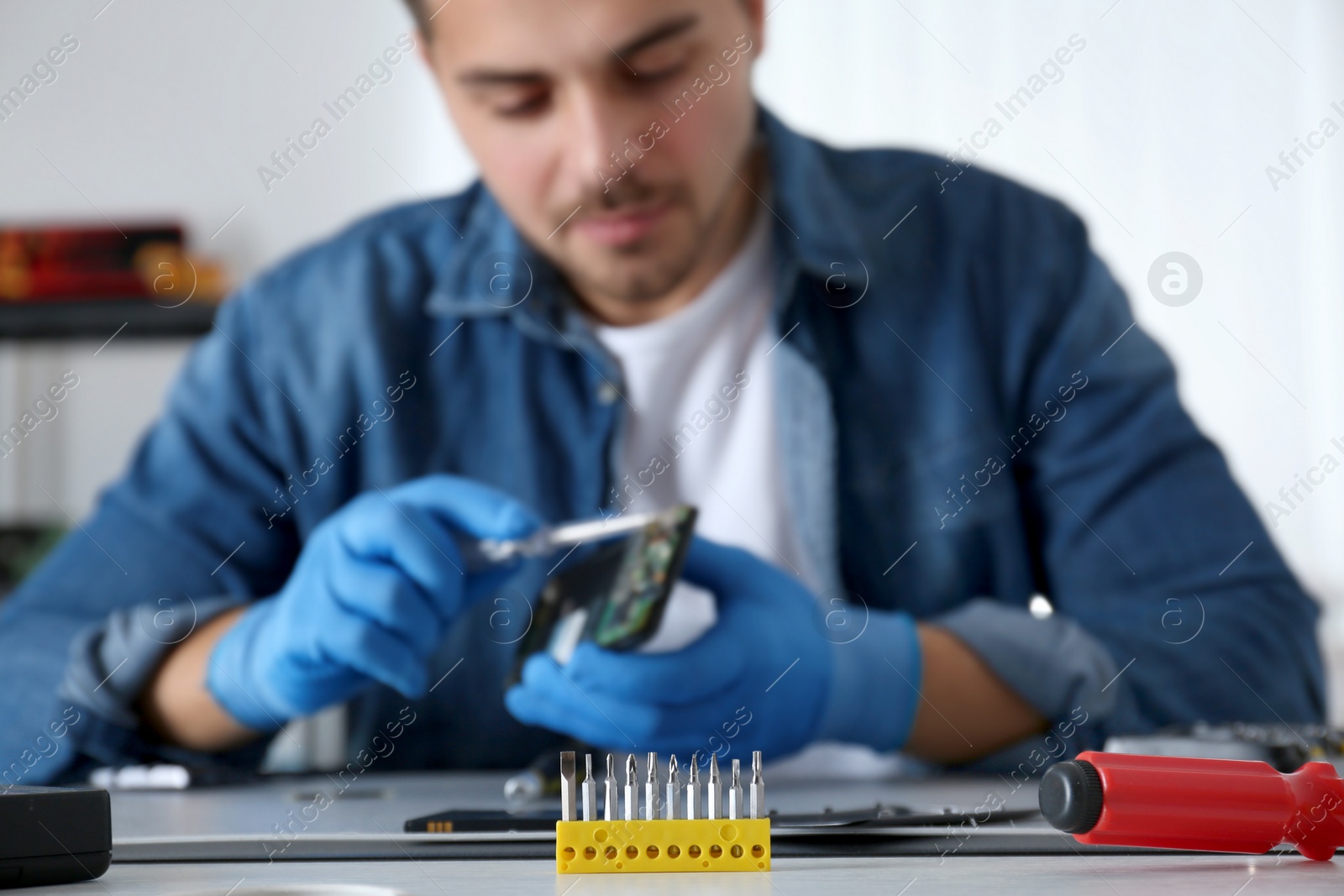 Photo of Technician repairing broken smartphone at table, focus on screwdriver security bits. Space for text