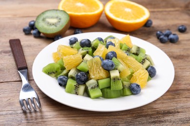 Photo of Plate of tasty fruit salad and fork on wooden table, closeup