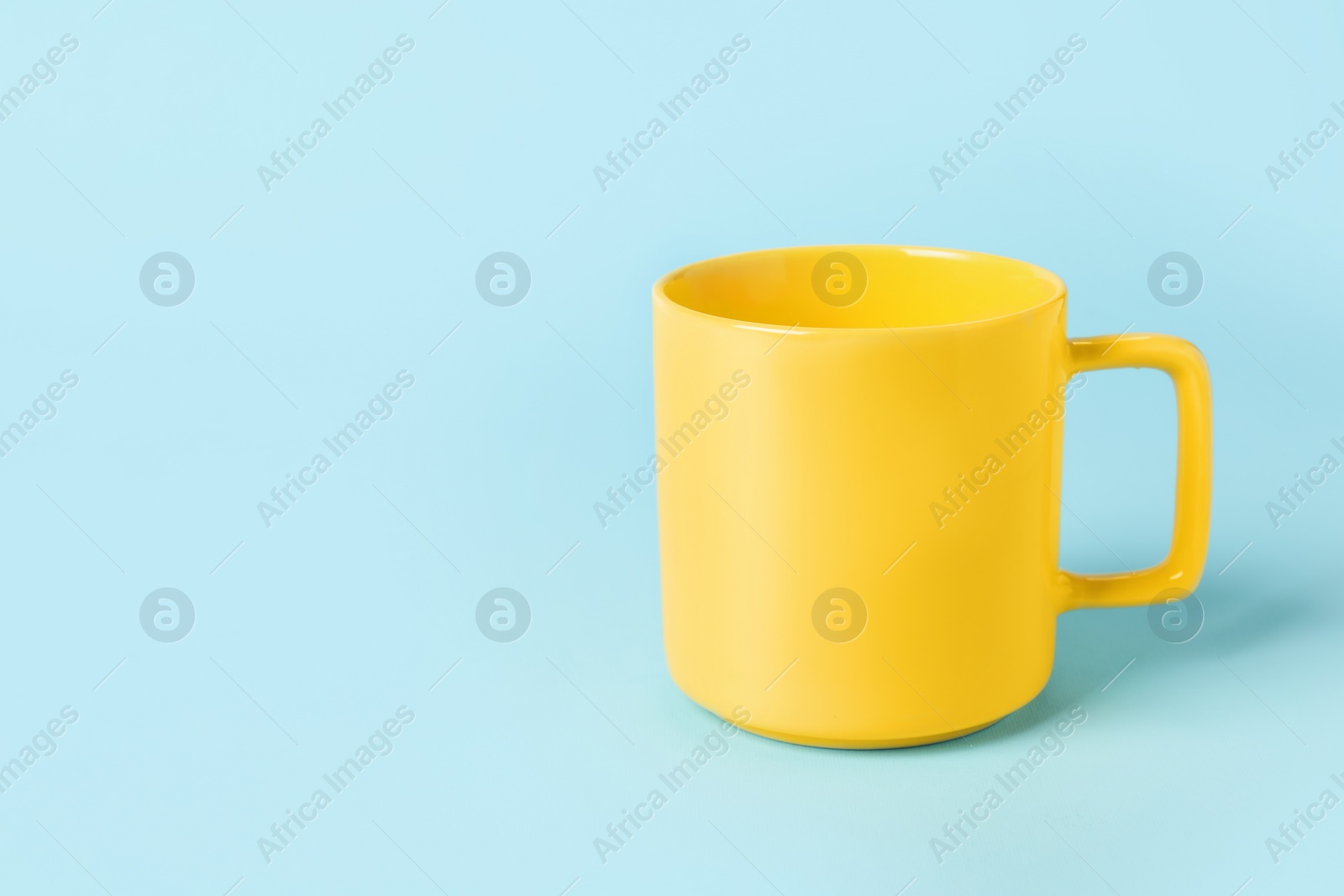 Photo of One yellow ceramic mug on light blue background, space for text