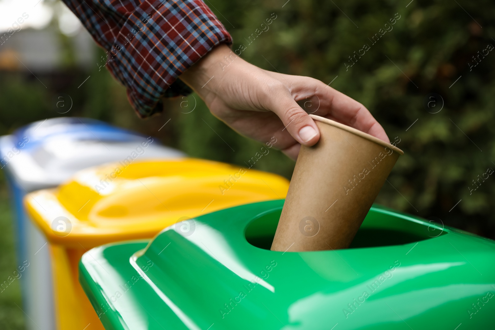 Photo of Woman throwing coffee cup into recycling bin outdoors, closeup