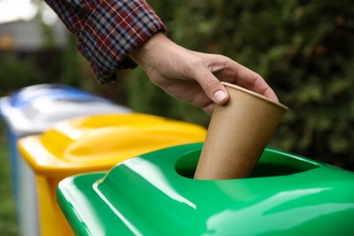 Woman throwing coffee cup into recycling bin outdoors, closeup