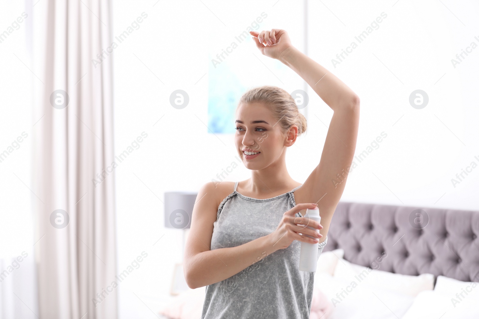 Photo of Beautiful young woman applying deodorant in bedroom