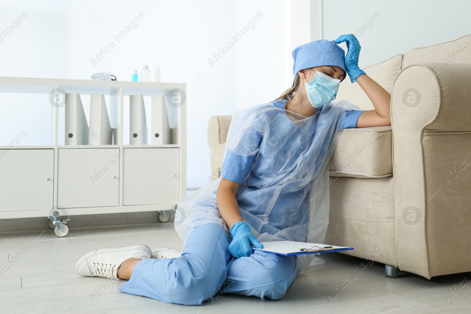 Photo of Exhausted doctor sitting on floor indoors. Stress of health care workers during COVID-19 pandemic