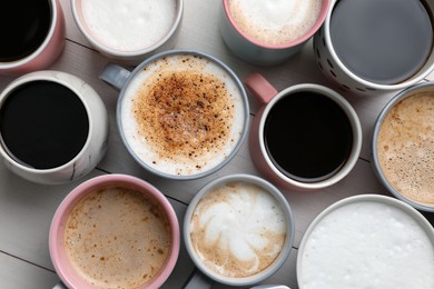 Many different cups with aromatic hot coffee on white wooden table, flat lay