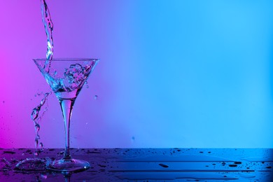 Photo of Pouring fresh martini into glass on table in neon lights, space for text