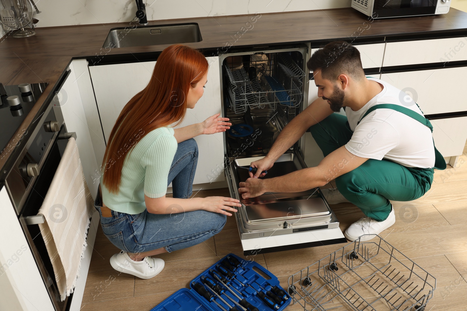 Photo of Woman looking how serviceman repairing her dishwasher in kitchen