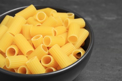 Photo of Raw rigatoni pasta in bowl on grey table, closeup