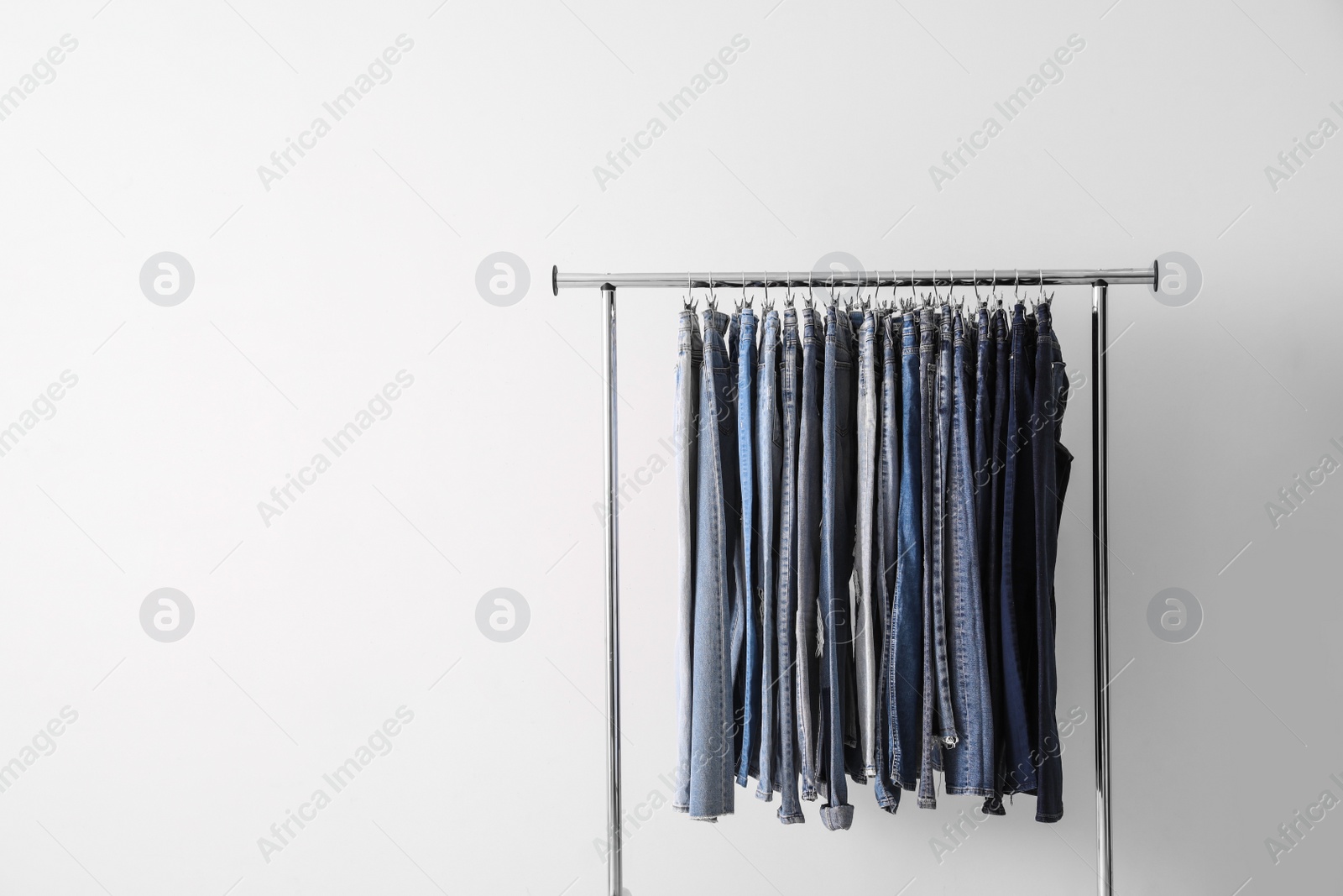 Photo of Rack with different jeans on light background. Space for text