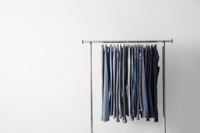 Rack with different jeans on light background. Space for text