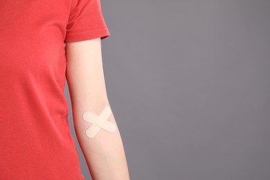 Photo of Blood donation. Woman with sticking plaster on her arm against grey background, closeup. Space for text