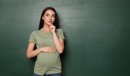 Pregnant woman near empty green chalkboard, space for text. Choosing name for baby