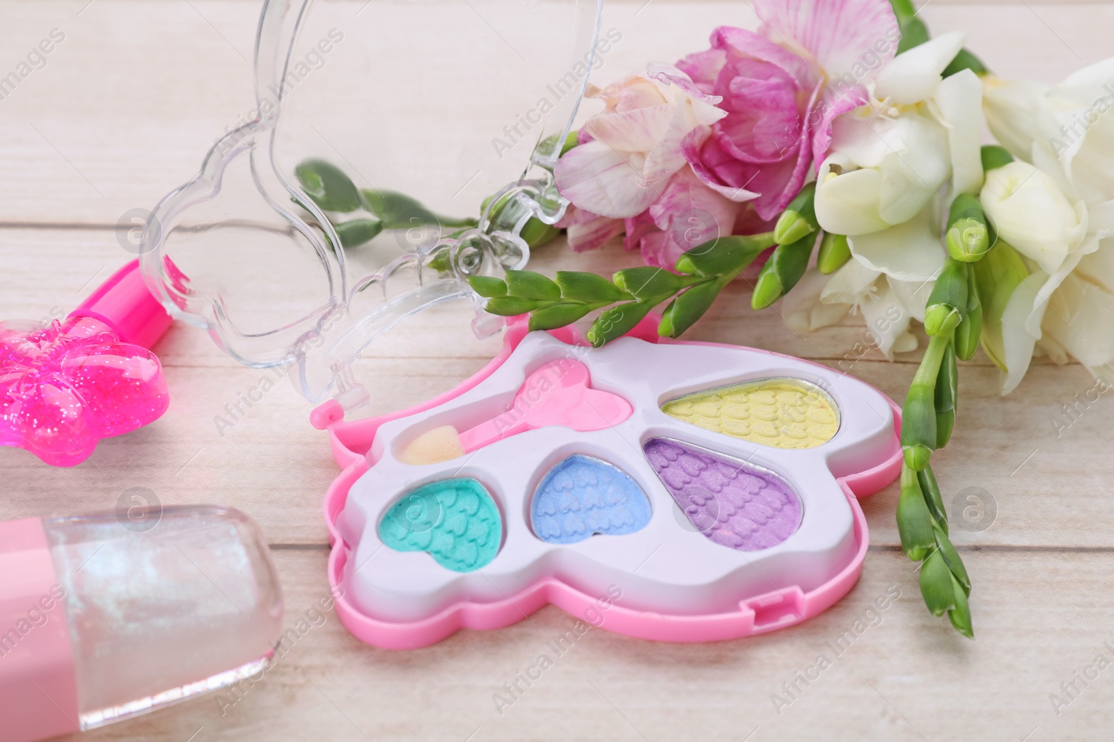 Photo of Decorative cosmetics for kids. Eye shadow palette, lipsticks and flowers on white wooden table, closeup