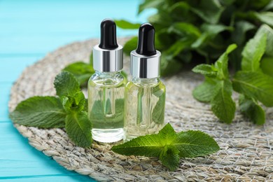 Photo of Bottles of essential oil and mint on turquoise wooden table, closeup